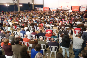 Ein volles Stadion mit vielen sitzenden und stehenden Menschen, eine B√ľhne mit zwei Rednern am Podium und zahlreichen Fahnen und Lichtern in der N√§he.