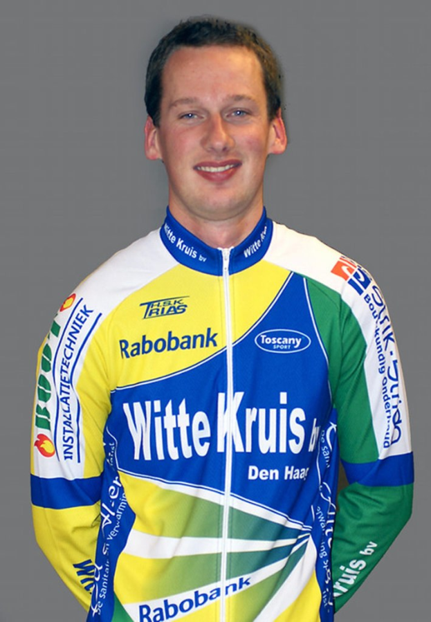 Ein männlicher Athlet posiert für ein Foto und trägt ein Shirt mit mehreren Sponsorenlogos.