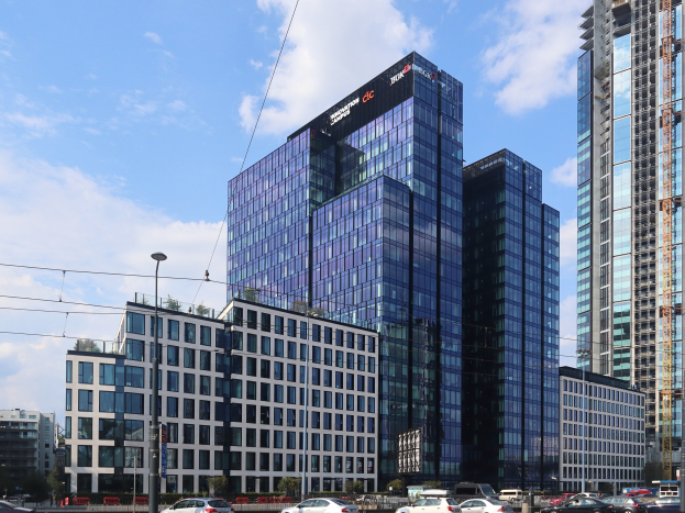 Zentrale der Deutschen Bank in Frankfurt, Deutschland, ein großes Gebäude mit vielen Fenstern, umgeben von städtischer Infrastruktur und Grün unter einem bewölkten Himmel.