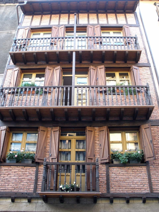 Ein mehrgeschossiges Gebäude mit zahlreichen Fenstern, Balkonen, Geländern, Türen und Blumentöpfen mit Pflanzen in Straßburg, Frankreich.