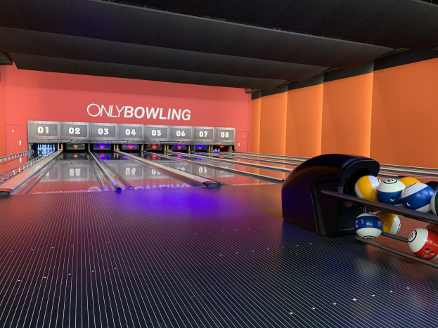 Eine Bowlinganlage mit Bowlingkugeln auf der rechten Seite, Bowlingkegel in der Mitte und einer textbedeckten Wand im Hintergrund, mit der Decke oben.