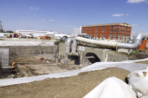 Eine Szene mit Gebäuden, einem Zaun, Fahrzeugen, aktuellen Umfragen, einem Rohr und einem Himmel darüber.