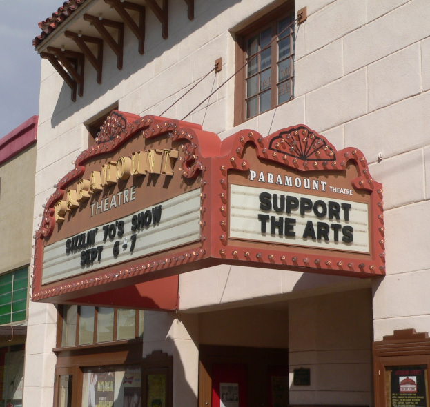 Außenansicht des Paramount Theatre in Sacramento, Kalifornien, mit Glasfenstern und -türen, einem "Unterstütze die Künste"-Schild und einem sichtbaren Himmel im Hintergrund.
