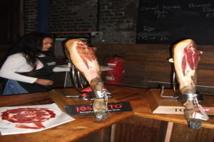 Eine Frau steht vor einem Tisch mit Fleisch darauf, mit Feuerlöscher und Anschlagtafel im Hintergrund.