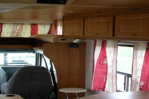 Ein Raum mit einem Tisch, Stühlen, einer Matte, Vorhängen und Fenstern.