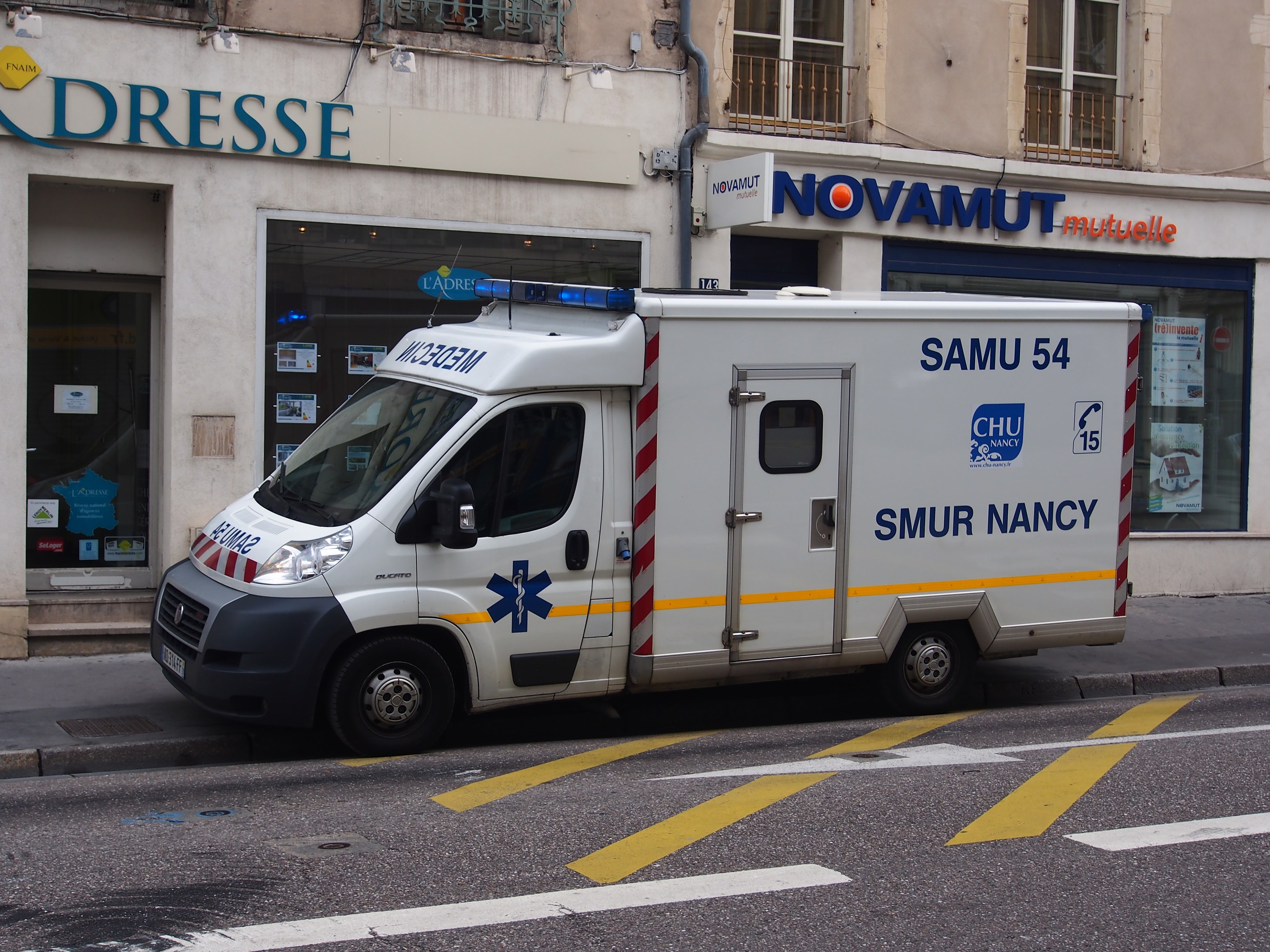 Rettungswagen vor einem Krankenhausgebäude mit Fenstern, Geländern und Informationsschildern geparkt.