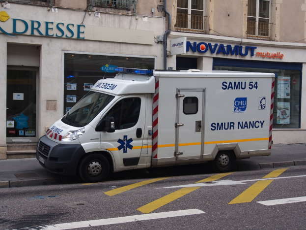 Rettungswagen vor einem Krankenhausgebäude mit Fenstern, Geländern und Informationsschildern geparkt.