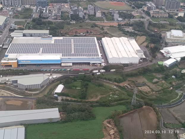 Luftaufnahme eines großen Industriegebiets mit Gebäuden, Bäumen, Gras, Straßen, Fahrzeugen, Masten und einem Wasserzeichen, das es sich um die erste Solarstromanlage in Singapur handelt.