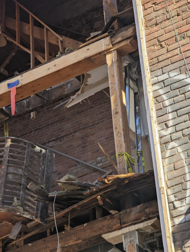 Ein teilweise abgerissener Bau mit verstreuten Holzplanken und Trümmern sowie zerbrochenen Fenstern und Türen.