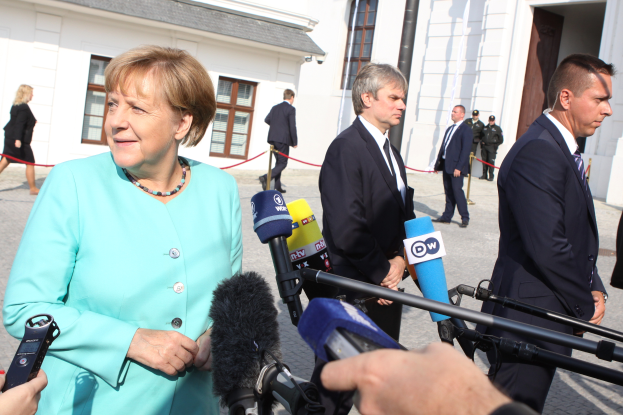 Bundeskanzlerin Angela Merkel spricht vor der Reichstag in Berlin mit Reportern und ist von Menschen mit Mikrofonen umgeben.