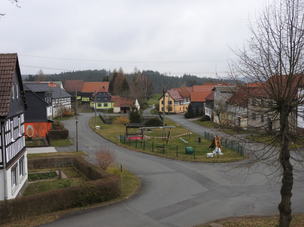 Kleinstädte mit Häusern, Straßeninfrastruktur, Fahrzeugen, Grünflächen, einem Spielplatz und einem klaren blauen Himmel.