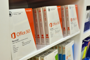 Ordentlich arrangierte Microsoft Office 365-Kartons auf einem weißen Regal mit dem Microsoft-Logo auf der Vorderseite, vor einem leicht unscharfen Hintergrund.