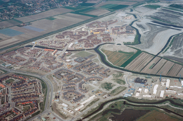 Luftaufnahme einer Stadt mit dichtem Baumbestand, Straßen, grünen Feldern, Bäumen und einem zentralen Reservoir, das von städtischen Gebieten umgeben ist.