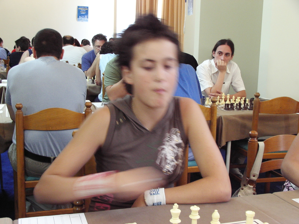 Ein Raum mit Menschen, die an Tischen Schach spielen, eine Vorhangwand mit einem Foto in der Ecke.