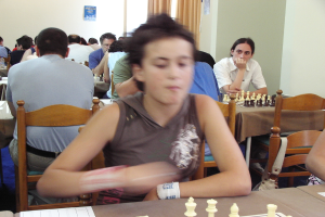 Ein Raum mit Menschen, die an Tischen Schach spielen, eine Vorhangwand mit einem Foto in der Ecke.