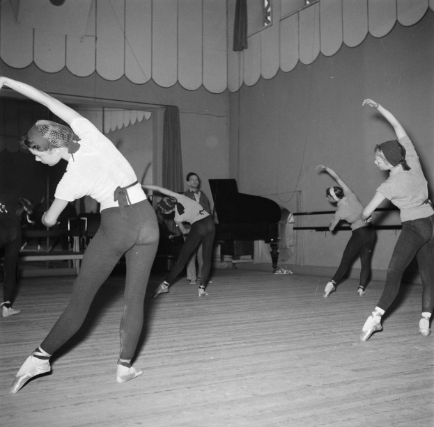 Schwarzes und weißes Bild einer Gruppe junger Frauen, die in einem Studio mit einem Piano und einer Wand im Hintergrund tanzen.