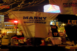 Eine Gruppe von Menschen in T-Shirts, die sich im Freien aufhalten, mit Ampeln, Bäumen, Pfählen und Gebäuden im Hintergrund.