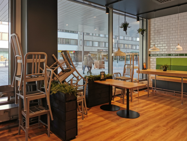 Ein Restaurantinnenraum mit hölzernen Tischen und Stühlen, große Fenster zeigen eine Berliner Straße mit Fußgängern, Gebäuden und urbanen Elementen.