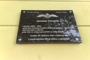 Schwarze Plakette mit weißer 'Jaroslav Chmelik'-Beschriftung und dekorativem Rahmen an einer Gebäudewand montiert.