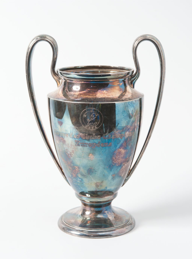 UEFA Champions League-Trophäe, ein stählerner Pokal mit zwei Griffen, in Blau und Silber gehalten, mit der Inschrift "UEFA Champions League", vor einem weißen Hintergrund dargestellt.