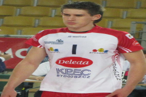 Ein Mann in einem roten und weißen Handballtrikot steht auf einem Feld, umgeben von Zuschauern, mit einem roten Banner im Hintergrund, das "Krasnoyarsk vs Bydgoszcz" lautet und entschlossen aussieht.