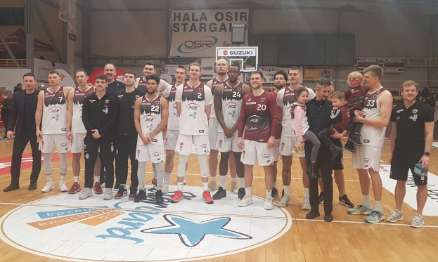 Gruppe von Männern und Kindern auf einem Basketballfeld mit Bannern, auf denen "Hala Osir Starga" steht.