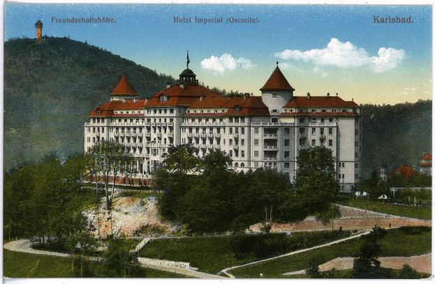 Alte Ansichtskarte des Hotels Imperial in Karlsbad, Deutschland, die ein großes Gebäude mit Fenstern zeigt, umgeben von Bäumen, Pflanzen, Gras, einem Pfad, einer Baumgruppe, Hügeln und einem bewölkten Himmel, mit Text oben.