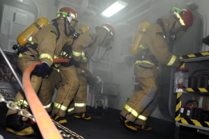 Feuerwehrleute in Schutzausrüstung arbeiten in der Nähe eines Feuerwehrautos mit einem Gestell von Gegenständen und Hintergrundrohren und -lichtern.