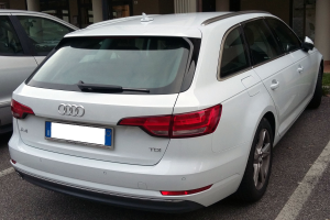 Ein weißer Audi A4 Avant 2.0 TDI Quattro Tiptronic S Tronic S Line steht auf der Straße vor einem Gebäude mit Glastüren und Säulen, rechts davon ist Gras.