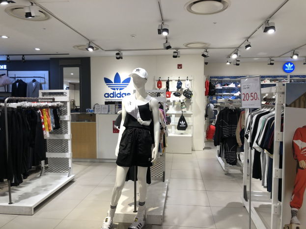 Innenansicht eines adidas-Geschäfts in Singapur mit Schaufensterpuppen, Kleiderauslagen, einem Textbrett auf der rechten Seite und Deckenleuchten.