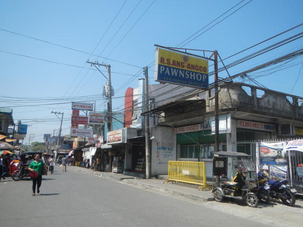 Eine belebte Straße mit Füülern, parkenden Motorrollern, Schildern an Gebäuden, überleitungen auf Masten und einem klaren blauen Himmel.