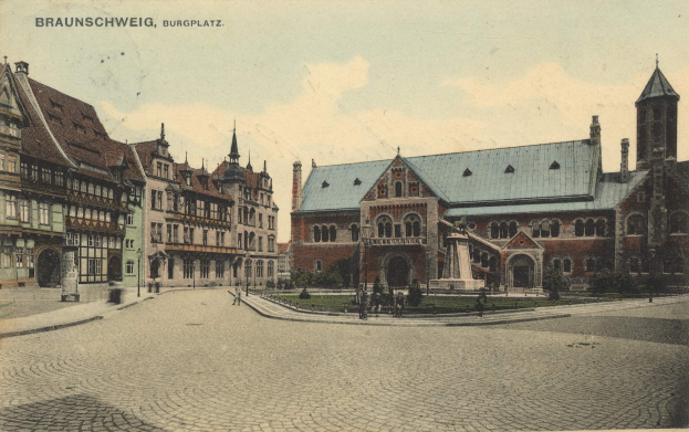 Eine alte Ansichtskarte, die den Burgplatz in Braunschweig, Deutschland zeigt, mit einer Gruppe von Gebäuden mit Fenstern, einer Statue auf einem Sockel, Menschen auf dem Boden, Pflanzen, Gras und einem bewölkten Himmel.