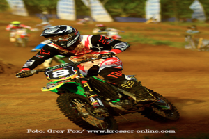 Mehrere Motorradfahrer mit Helmen auf einer Rennstrecke, mit Text am unteren Bildrand.