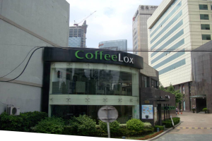 Ein Geschäftsgebäude mit einigen Pflanzen davor, umgeben von vielen hohen Gebäuden und Überlandleitungen.