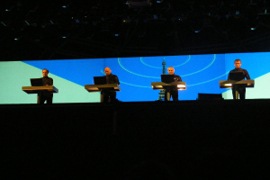 Vier Männer auf individuellen Podesten, jeder mit einem Laptop, vor einem großen Eiffelturm-Gebäude.