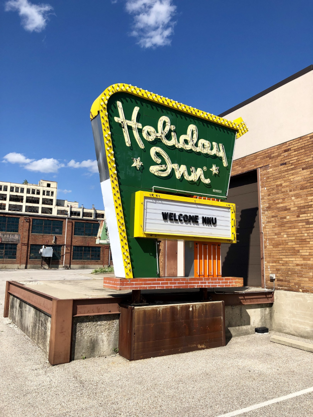 Holiday Inn-Schriftzug an einem Gebäude mit einem Textschild davor, bewölkter Himmel und sichtbare Fenster im Gebäude.