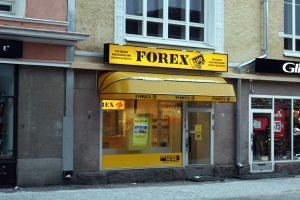 Ein Forex-Geschäft mit Glaswänden und Fenstern an einer Straßenecke, das Schilder mit Texten zeigt.