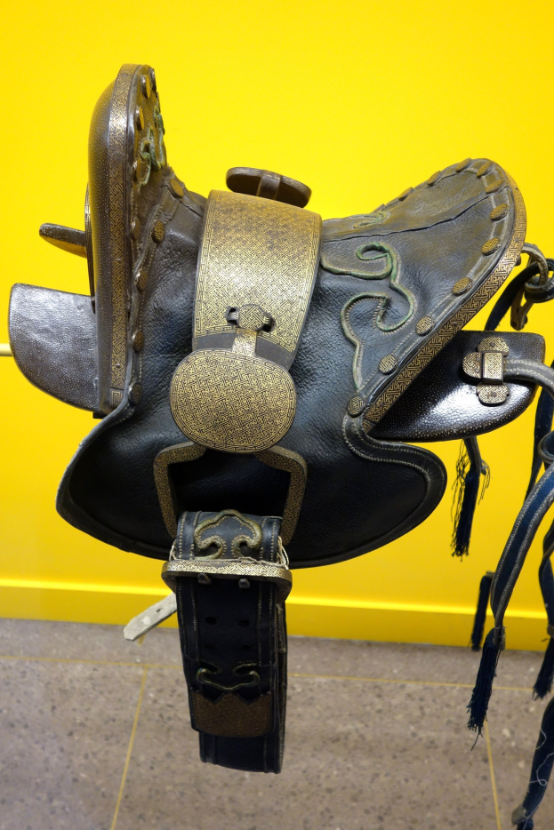 Nahaufnahme eines Pferdesattels, der auf einer gelben Wand mit dem Boden darunter angezeigt wird.