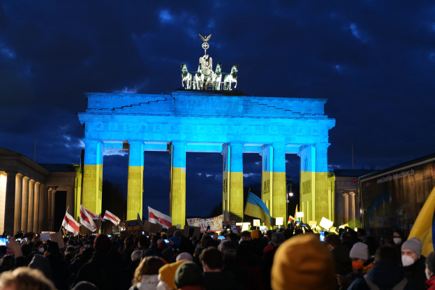 Menge mit Fahnen und Plakaten vor dem Brandenburger Tor in Berlin, mit einer Banner auf der rechten Seite des Bildes.
