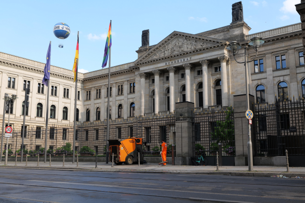 Großes Gebäude mit zahlreichen Fenstern, als Bundestag in Berlin, Deutschland identifiziert, umgeben von Straßeninfrastruktur, Fußgängern, Fahrzeugen und Bäumen unter einem bewölkten Himmel.