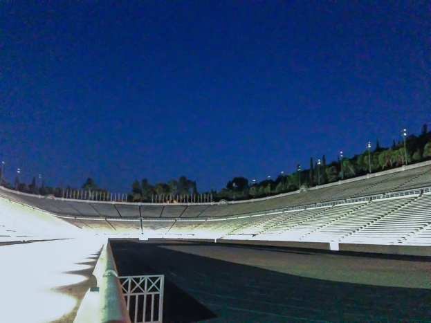 Olympiastadion bei Nacht, beleuchtet von Stadionlichtern und Sternen, umgeben von Bäumen und Pfählen und dem Boden unten sichtbar.
