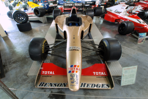 Rennwagen im Motorsportmuseum ausgestellt, durch einen Metallzaun von Besuchern im Hintergrund getrennt.