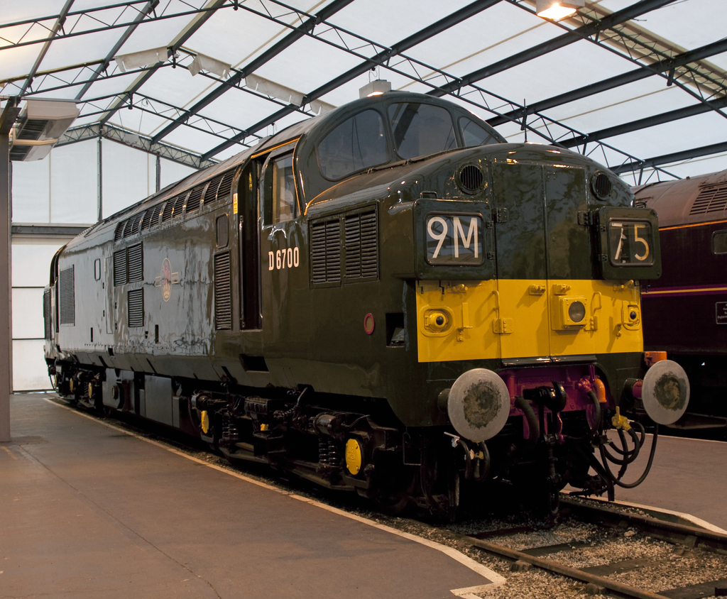 Ein Zug befindet sich auf den Schienen neben einer Plattform mit einem Mast auf dem Dach, der Metallstangen mit Lampen trägt.