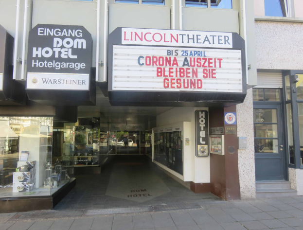 Das Lincoln Theater in Berlin, Deutschland, mit Glasfenstern und -türen und einer Tafel davor sowie einem geschäftigen Inneren mit verschiedenen Gegenständen.