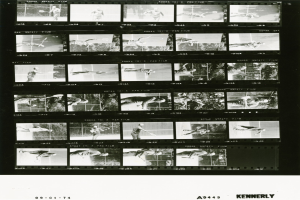 Ein Schwarz-Weiß-Foto eines Mannes in einem weißen Hemd und Shorts, der konzentriert Tennis spielt und einen Filmstreifen im Hintergrund hält.