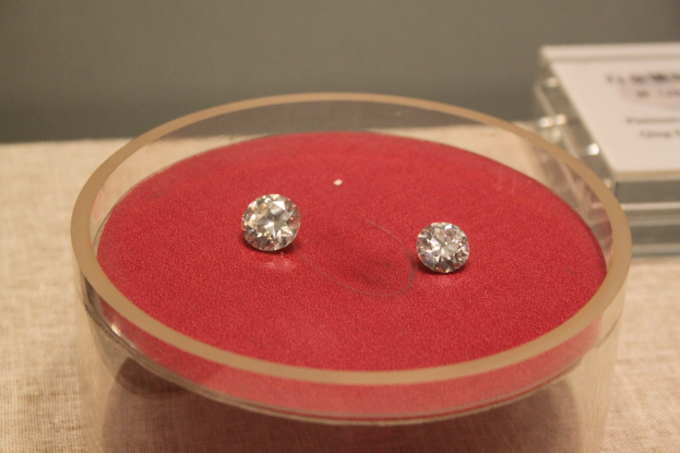 Ein Paar Diamant-Ohrringe in einer durchsichtigen Glasbox auf einem Tisch, funkelnd und das Licht reflektierend.