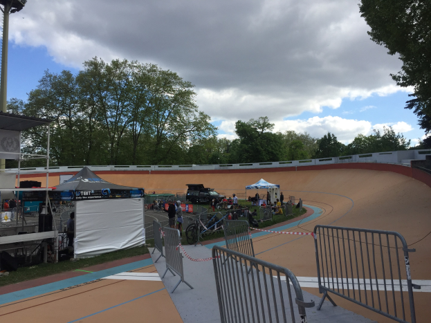 Gruppe von Radfahrern auf einer Schmutzspur bei einem Outdoor-BMX-Event mit Zelten, Fahrzeugen und Bäumen im Hintergrund.