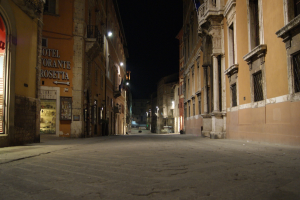 Eine Nachtansicht einer Stra├če mit Geb├Ąuden auf beiden Seiten, einem Laden auf der linken Seite und Lichtern in der Mitte.