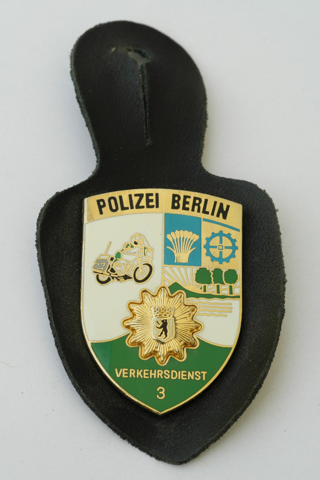 Ein schildförmiges Polizeibadgen mit "Polizei Berlin" in schwarzer Schrift, das ein weißes Stern auf einem blauen Hintergrund und einen weißen Rand hat, auf einer Oberfläche platziert.
