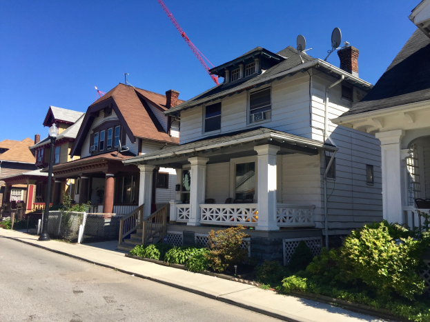 Reihe von Höusern mit verschiedenen architektonischen Details, ein Baukran auf einem Dach, ein Straßenpfahl, Pflanzen, ein Zaun.